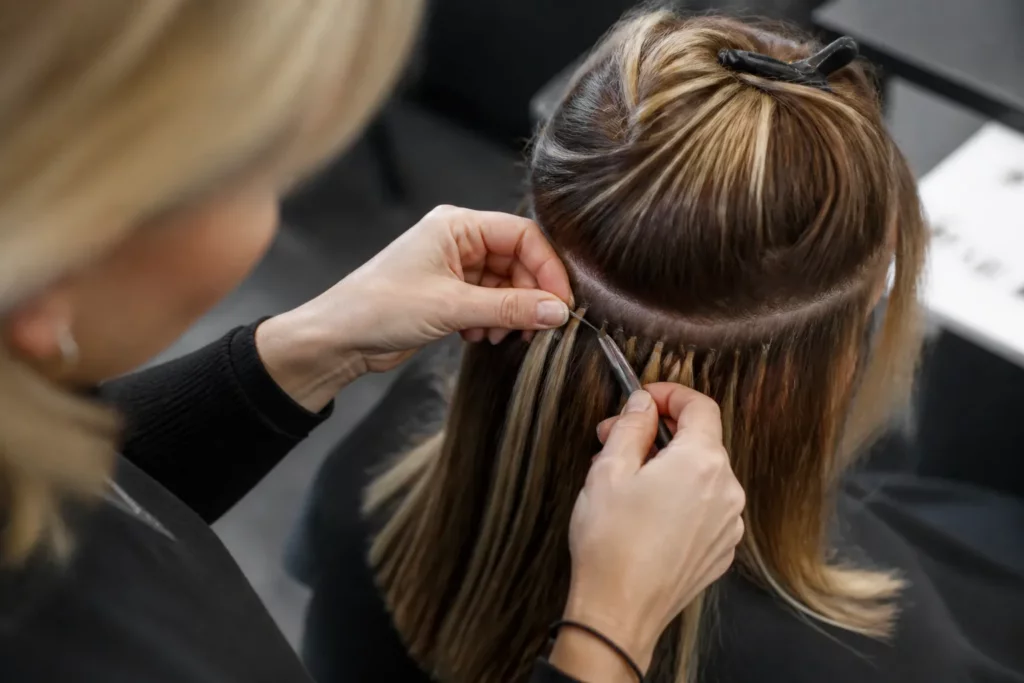 kapster die zorgvuldig hair extensions bevestigt in halflang haar in een moderne salon