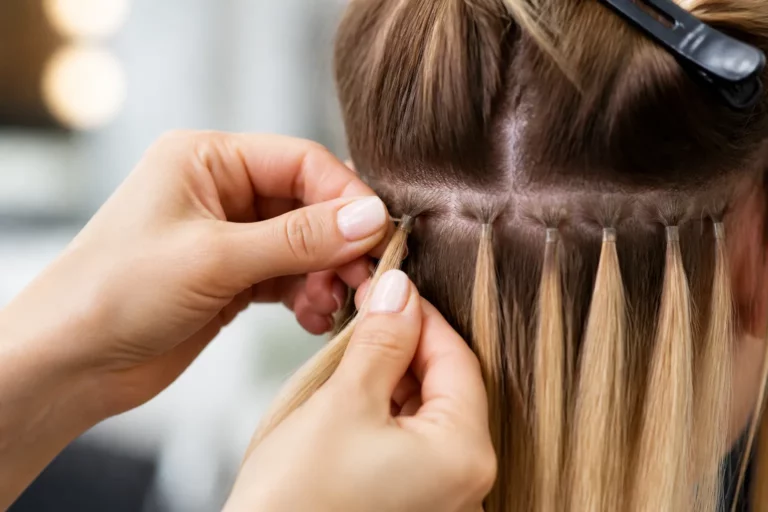 kapper zet hair extensions in gescheiden haarstrengen terwijl naastgelegen werkplek een andere haarbehandeling toont